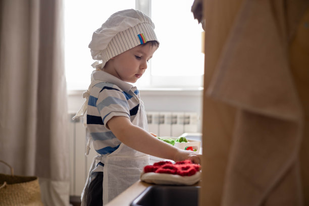 可爱的小男孩在厨师帽和围裙玩孩子气的厨房烹饪食物的背影图片下载