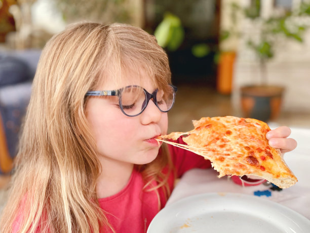 小女孩正在吃披萨。快乐的孩子咬着奶酪披萨。图片下载