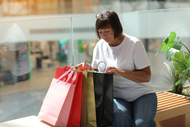 在精品店的背景下，一名快乐的成年女性在购物中心购物后，正看着里面的彩色购物袋。时尚和购物理念。黑色星期五促销图片下载