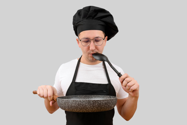 年轻的厨师戴着一顶帽子，手里拿着一只煎锅，孤零零地出现在蓝色的背景上。烹饪和人的概念图片下载