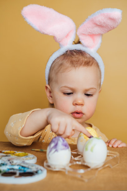一个头上戴着兔子耳朵的孩子在画复活节彩蛋图片下载