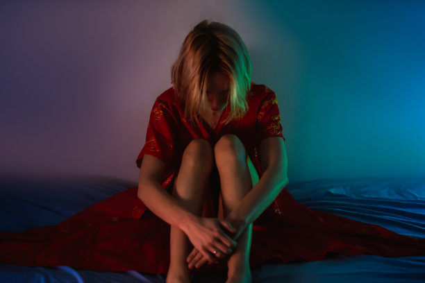 女性的思想，危机。一个穿着红色长袍的面目全非的女人低着头坐在床上。图片下载