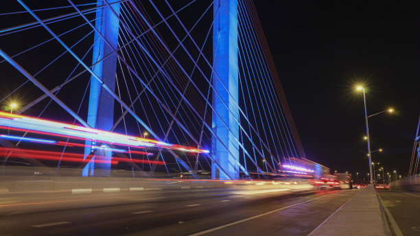 吊桥在蓝色照明与白色，蓝色和红色的汽车灯在夜间高速公路上。长时间的曝光。视平线图片下载