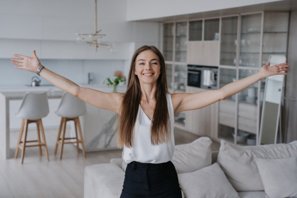 开朗的白人年轻女子随意摊开双手站在客厅欢迎拥抱。满意的意大利女孩对新公寓感到高兴，庆祝拥有。房地产经纪人介绍公寓图片下载