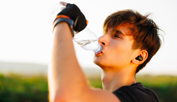 男子在海滩跑步锻炼后喝水。口渴的健康男性，身体健康，喝水。图片下载