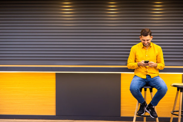 帅气自信时尚潮男模特。性感的现代男人穿着优雅的米色西装。日落时分，时尚男性在城市木栅栏附近的街道上摆姿势图片下载