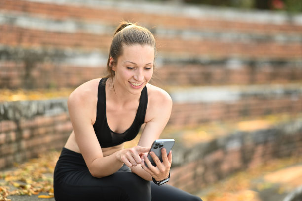 微笑的年轻女运动员在户外楼梯上放松时使用智能手机。健身、运动、健康生活理念。图片下载