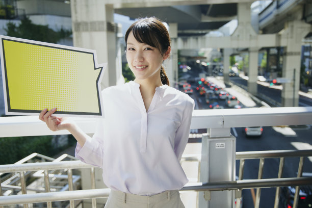 一名亚洲妇女在人行天桥上举着一个空的演讲泡泡。图片下载