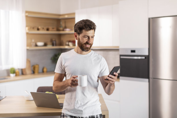 穿着白t恤、留着胡子、神情忧郁的中年白人男子，一边喝着杯子里的饮料，一边在智能手机上阅读信息图片下载