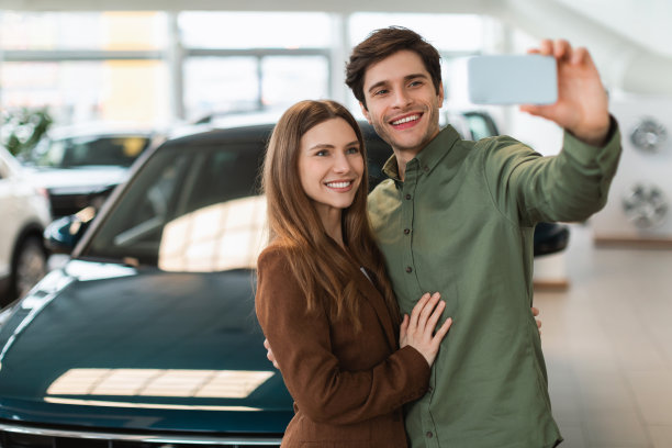 快乐的年轻夫妇在汽车经销店用智能手机自拍，复制空间图片下载