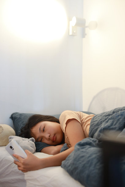 年轻的亚洲女孩醒来，看着她的智能手机。图片下载