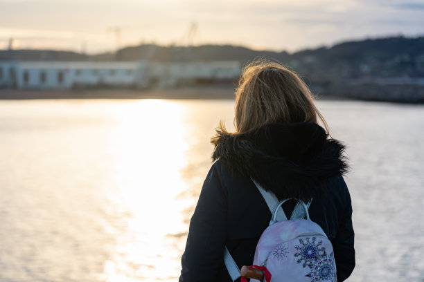 在一个晴朗的冬日，西班牙希洪，一名女子凝视着大海，享受着阳光。图片下载