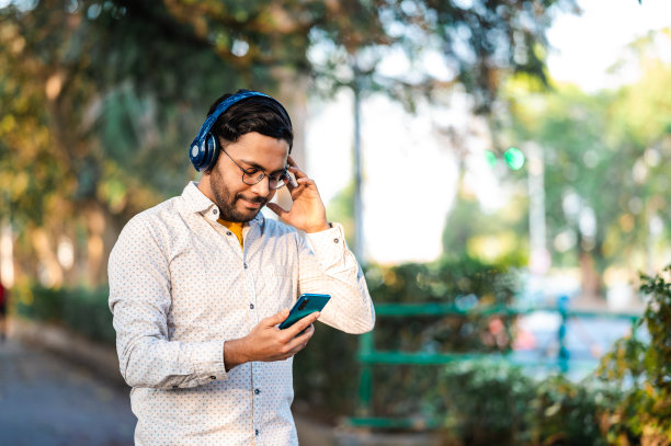 微笑的年轻有魅力的男人听音乐在城市的街道图片下载