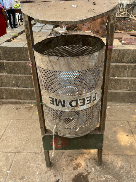 近距离图像的圆柱形，生锈的金属垃圾桶在铺好的天井区域，“喂我”的标志在垃圾桶的金属框架与屋顶，重点在前景图片下载