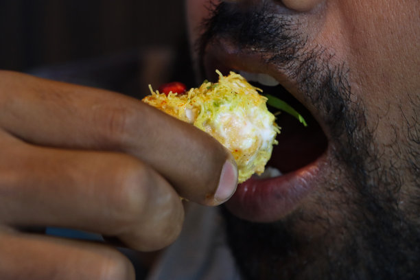 特写照片，一个认不出来的人满嘴吃着茶点，拿起golgappa puri(油炸水球)，空心酥脆的球体，里面有土豆、洋葱、石榴籽、辣味酸辣酱、Dahi papri chaat、酸奶和Sev图片下载