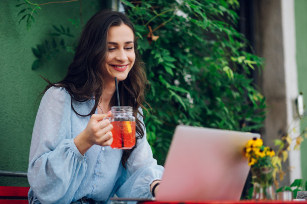 一名女子坐在街边咖啡馆边喝冷饮边用笔记本电脑图片下载