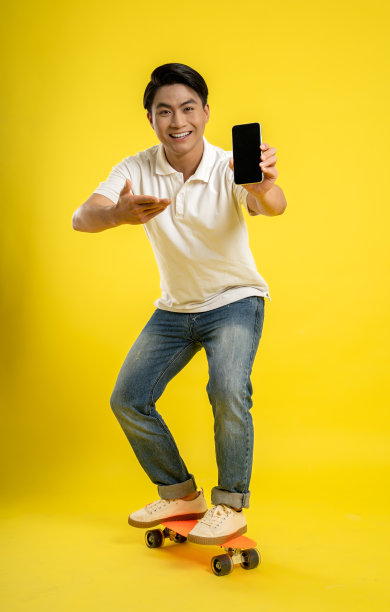 黄色背景下的亚洲青年使用手机和玩滑板的图片图片下载