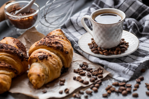 美味的现烤牛角包，黑色背景是巧克力和咖啡。法国早餐。美味的糕点特写。面包店里有美味的面包。糖果产品。图片下载