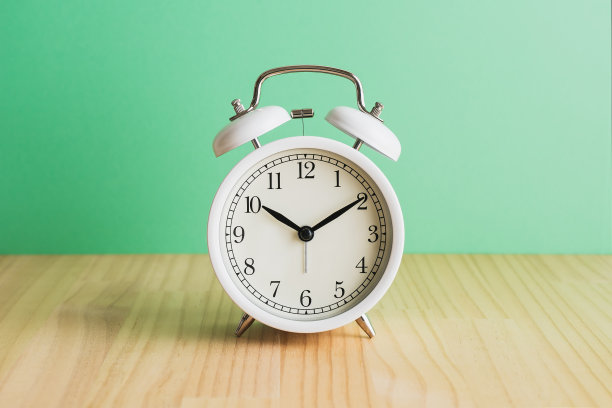 白色闹钟，绿色背景的木桌。图片下载