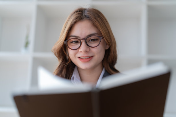 特写漂亮的年轻女子戴眼镜读书。图片下载