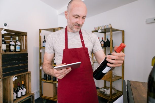 成熟的卖家在酒庄拿着一瓶酒用平板电脑-注意面部图片下载