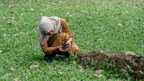女子在草地上用智能手机拍照。自然和绿色背景。图片下载