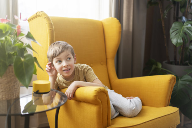 一个小男孩坐在椅子上和一个聪明的扬声器交流图片下载