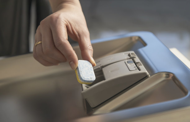 一只手把胶囊放进洗碗机的容器里。洗碗的概念。图片下载