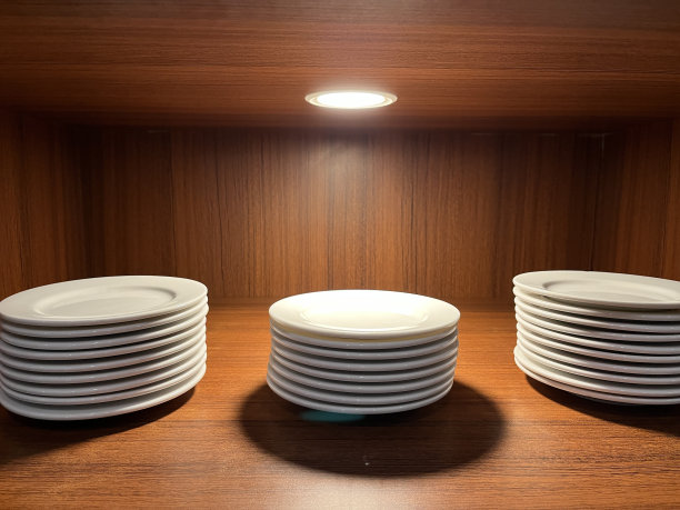 一堆白色的盘子在一个有聚光灯的木柜子里图片下载