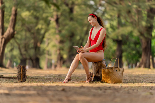 美丽的白人女性性感的女人在红色泳衣比基尼自拍与一个数字平板电脑，戴着太阳镜和一个红色的头带微笑凉爽和放松快乐的森林在海滩图片下载