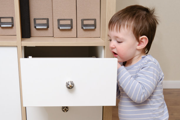 蹒跚学步的婴儿打开橱柜抽屉。小孩在家里客厅玩衣柜。孩子一岁九个月大图片下载