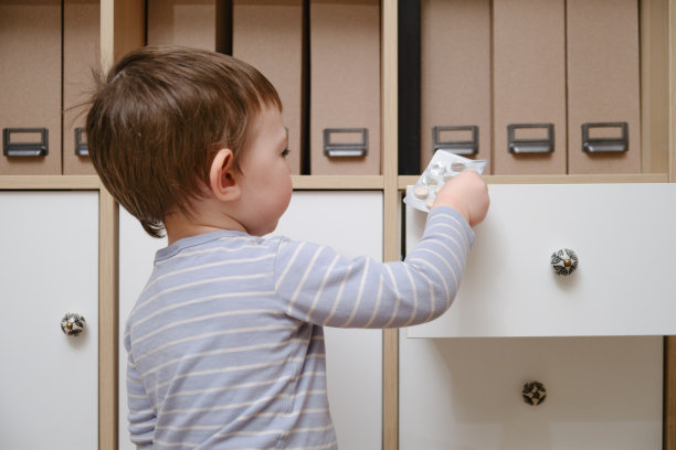 蹒跚学步的婴儿打开橱柜抽屉，里面放着药丸和药品。小男孩在家里客厅里拿着一包药。孩子一岁九个月大图片下载