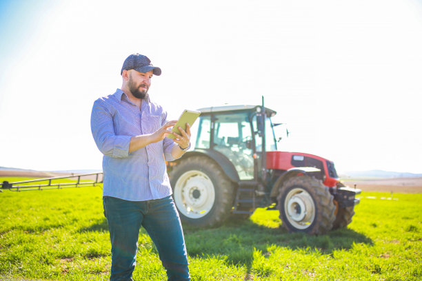 快乐的年轻农民在一辆红色拖拉机前用平板电脑做智能农业。智能农业概念图片下载