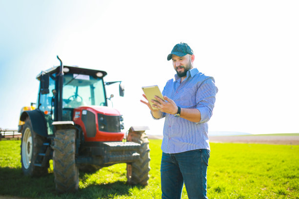 快乐的年轻农民在一辆红色拖拉机前用平板电脑做智能农业。智能农业概念图片下载