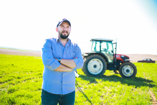 快乐的年轻农民双臂交叉在红色拖拉机前图片下载