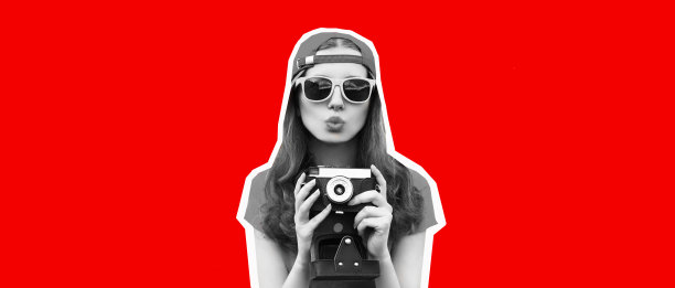 快乐的年轻女子摄影师的肖像用胶片相机拍照，吹她的嘴唇戴着棒球帽在红色的背景，杂志风格图片下载