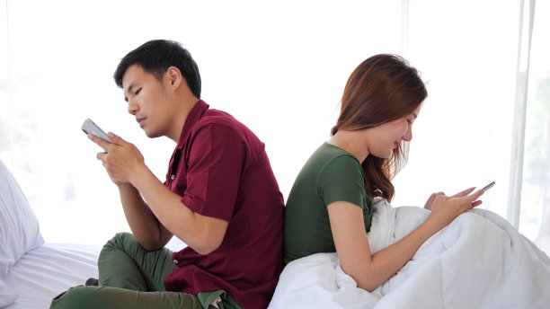 一对亚洲情侣坐在床上，用手机发短信，背对着对方，用智能手机。冷漠与不重视彼此图片下载