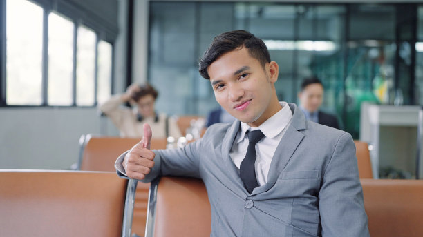 帅气的亚洲商人穿着西装竖起大拇指庆祝工作的好消息坐在飞机上的座位上，看着飞机上的镜头图片下载