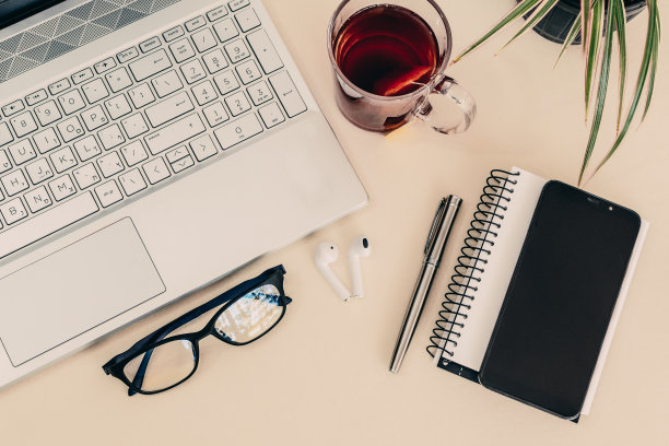 白色的桌子上有笔记本电脑、笔记本、一杯茶、耳机和眼镜的俯视图特写图片下载