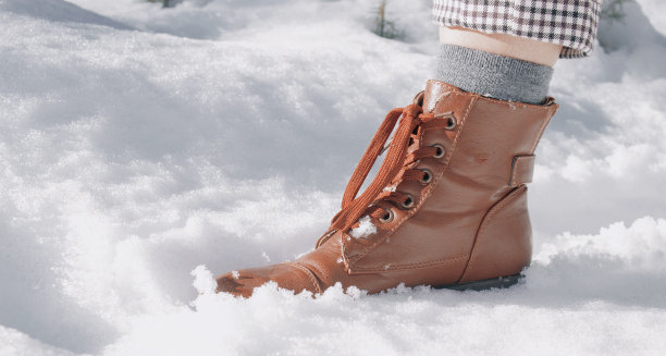 选择性聚焦拍摄了一位女性在雪地上的脚，穿着棕色皮靴，袜子，裤子图片下载