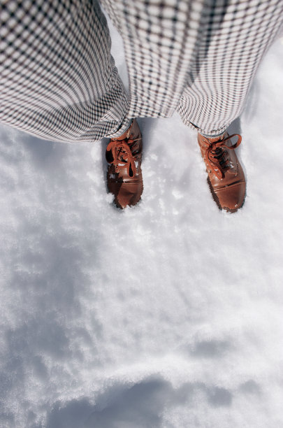 一个穿着黑白裤子和棕色靴子的女性站在雪地上的垂直镜头图片下载