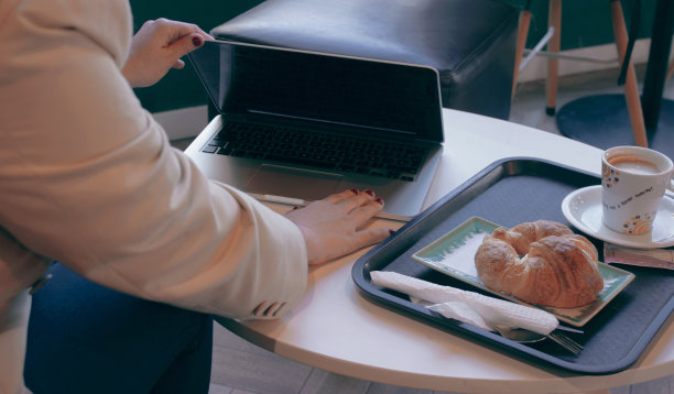 一位女士在早餐旁边的桌子上打开笔记本:羊角面包和咖啡图片下载