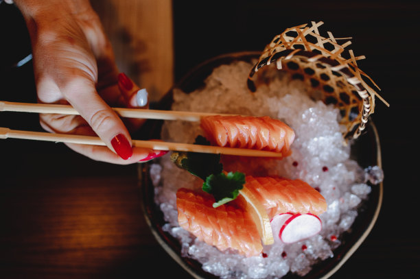 俯视图一个女人的手拿着日本刺身鲑鱼筷子放在一个黑色的盘子里图片下载