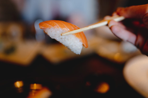 一个人在餐厅用筷子拿寿司的特写，背景模糊图片下载