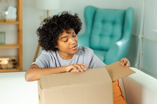 非洲女孩打开包裹看箱子。快乐的女人打开纸箱。女性拿包裹看交付的货物项目。满意客户积极反馈，快递快捷。图片下载