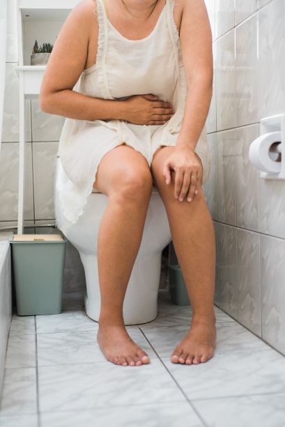 一个腹泻的妇女坐在她浴室的马桶上的垂直图像。图片下载