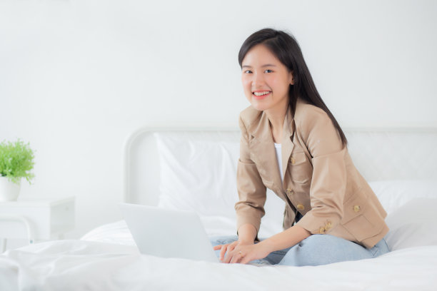 年轻漂亮的亚洲女人坐在床上使用笔记本电脑在卧室里在家工作，女性是自由职业者使用笔记本电脑在线，一个人，业务和生活方式的概念。图片下载