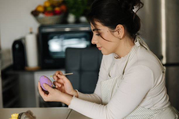 迷人的年轻女子用画笔画复活节彩蛋的紫色。春天的假期。图片下载