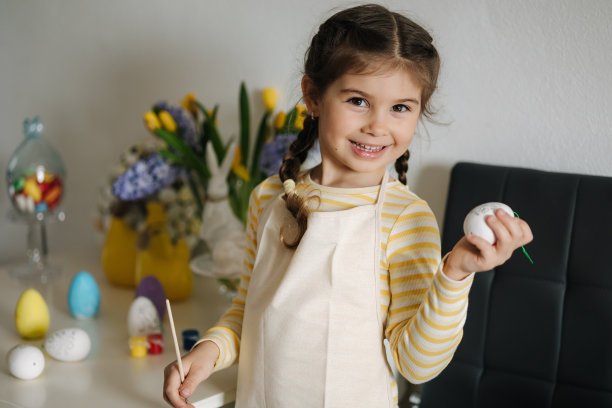 可爱的微笑的女孩手里拿着画笔和鸡蛋，准备画画。复活节厨房装饰图片下载