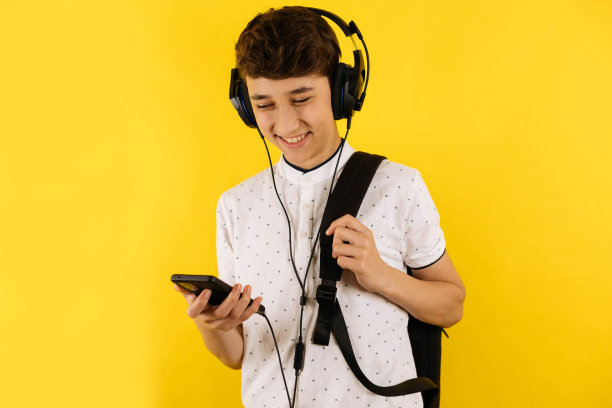 一个年轻的学生背着书包、智能手机和耳机。图片下载